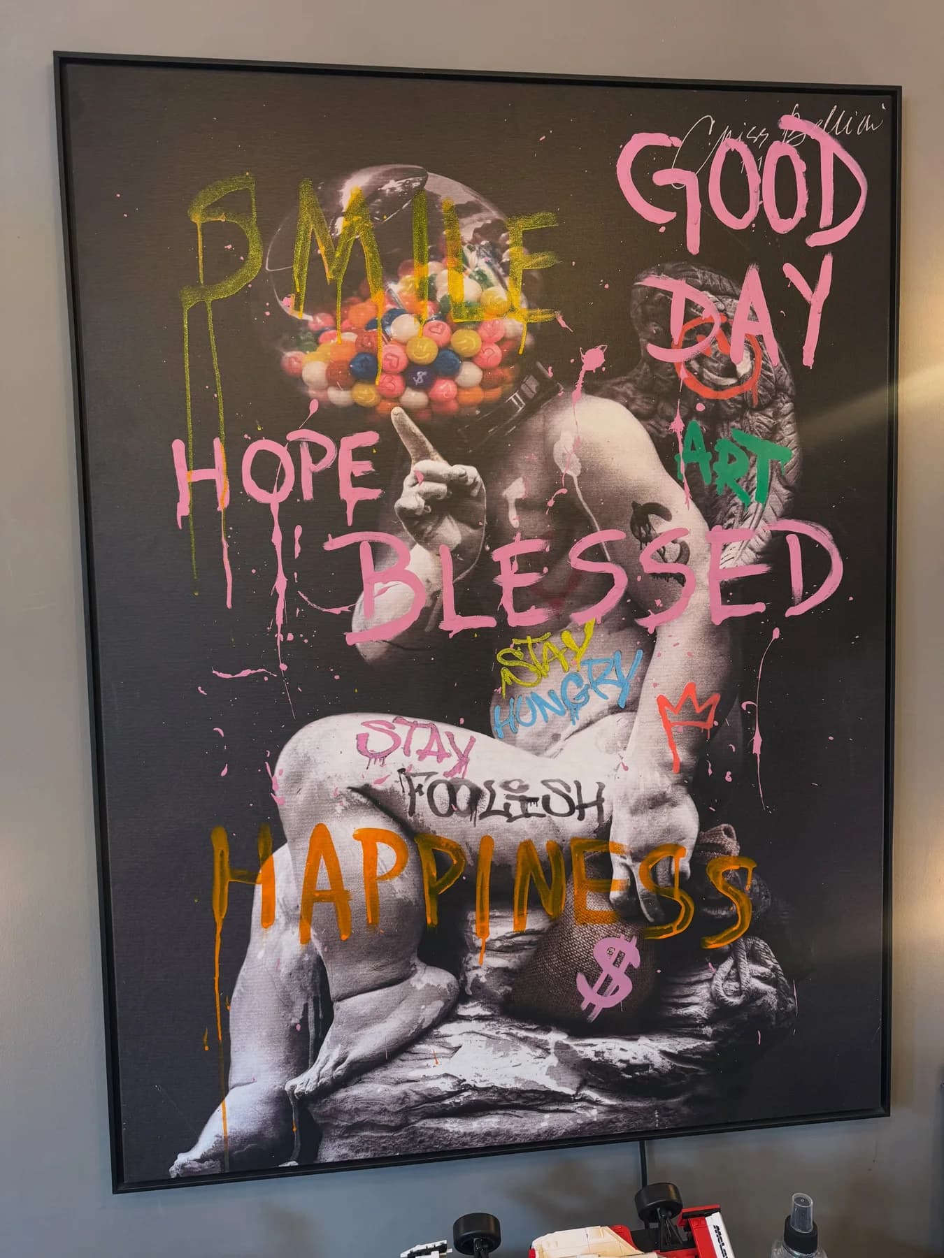 Quadro preto e branco de uma escultura clássica coberto de palavras grafitadas em rosa e laranja, como good day e blessed