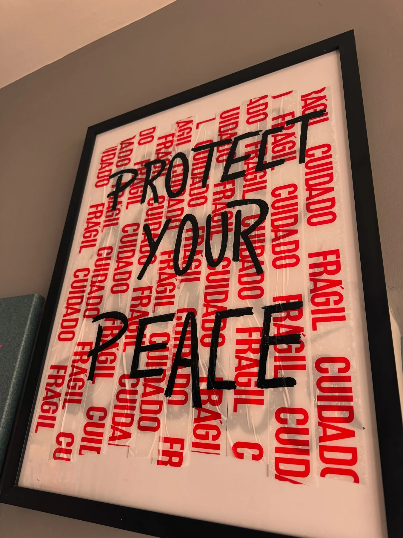 Quadro de moldura preta com fita de frágil vermelha ao fundo e a frase protect your peace em preto