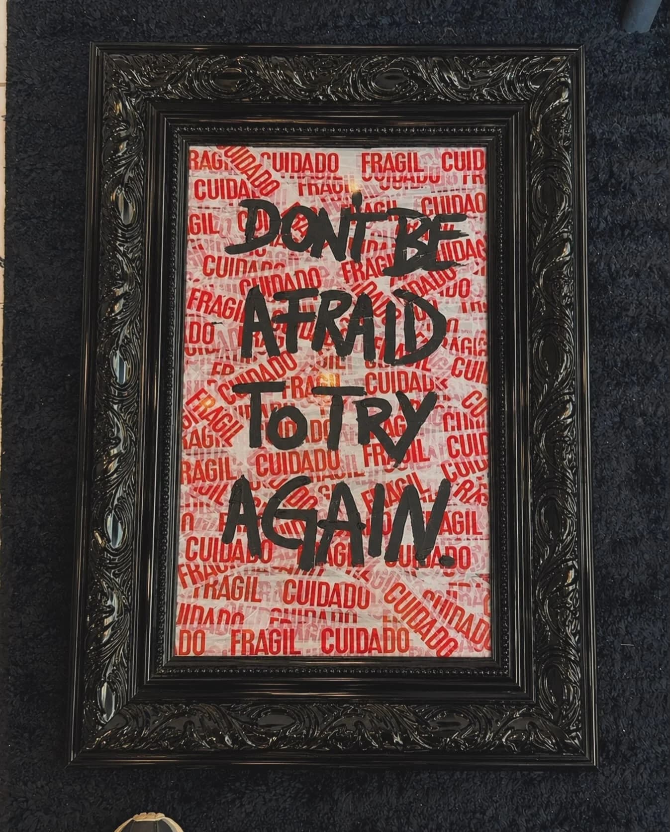 Quadro de moldura preta entalhada com fita de frágil vermelha ao fundo e a frase don't be afraid to try again em preto